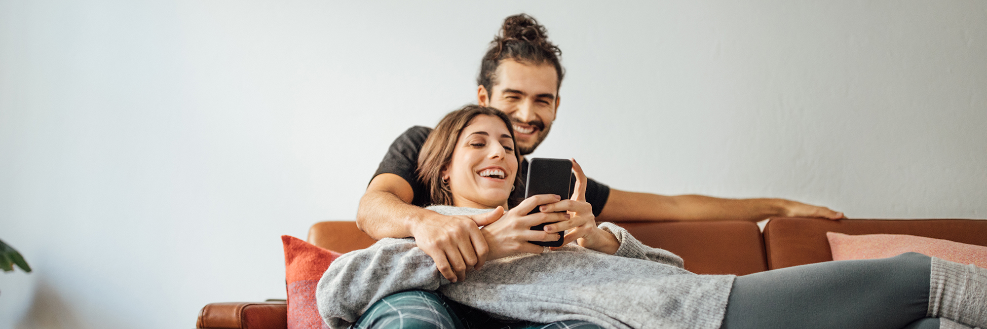 young woman laying on a sofa with a young man behind her both smiling looking at her smartphone  | Digital Wings blog | What is streaming
