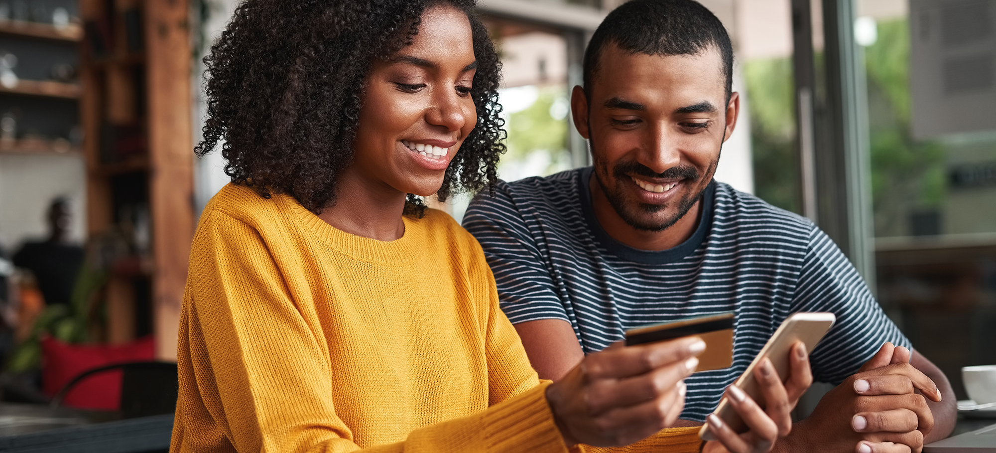 man and woman smiling sitting next to each other as she's holding a smart phone and a payment card | Digital Wings | Safe online shopping