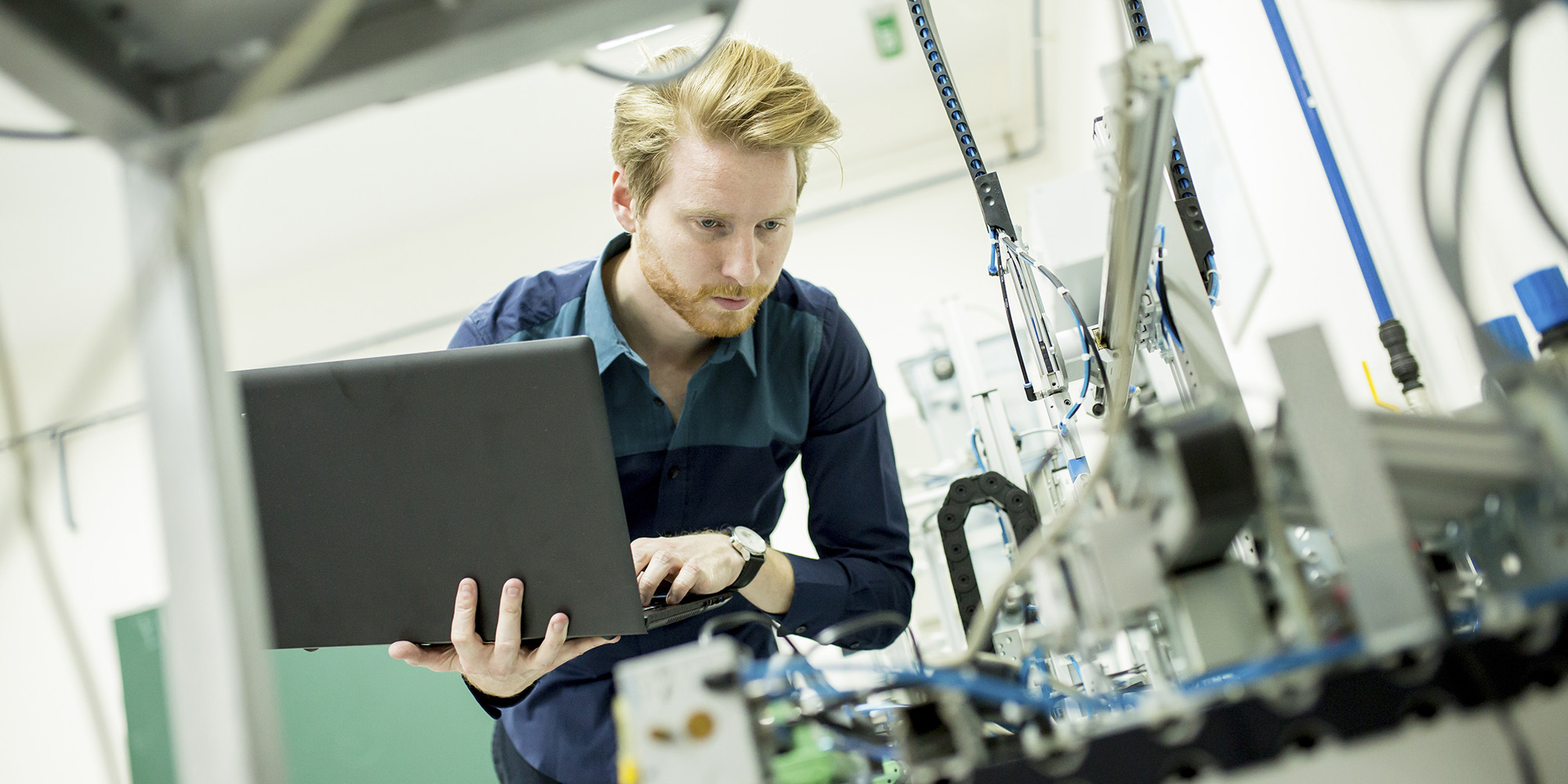 Man holding a laptop in front of some machinery