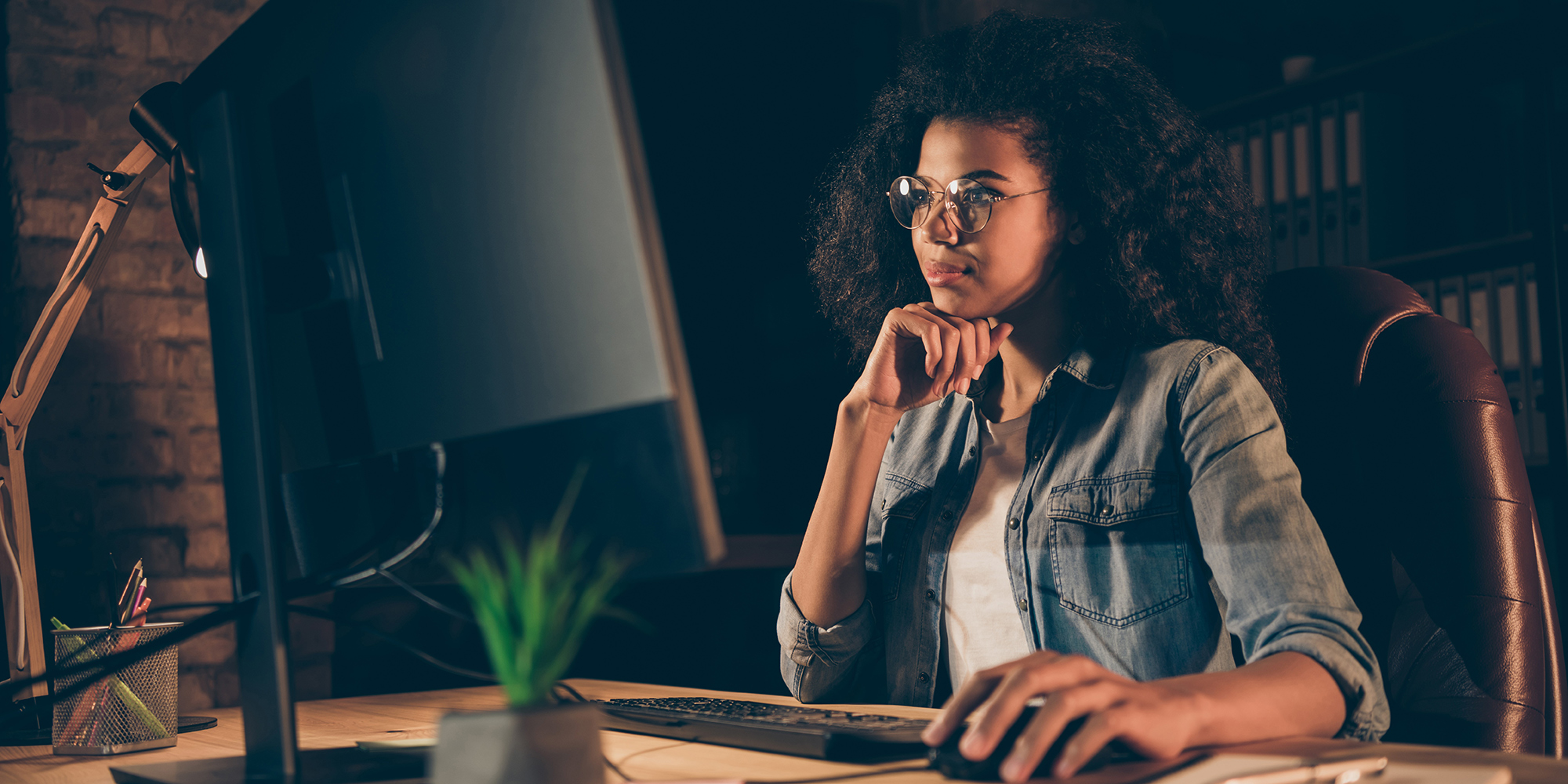 woman sitting in a dark room looking at her desk top computer