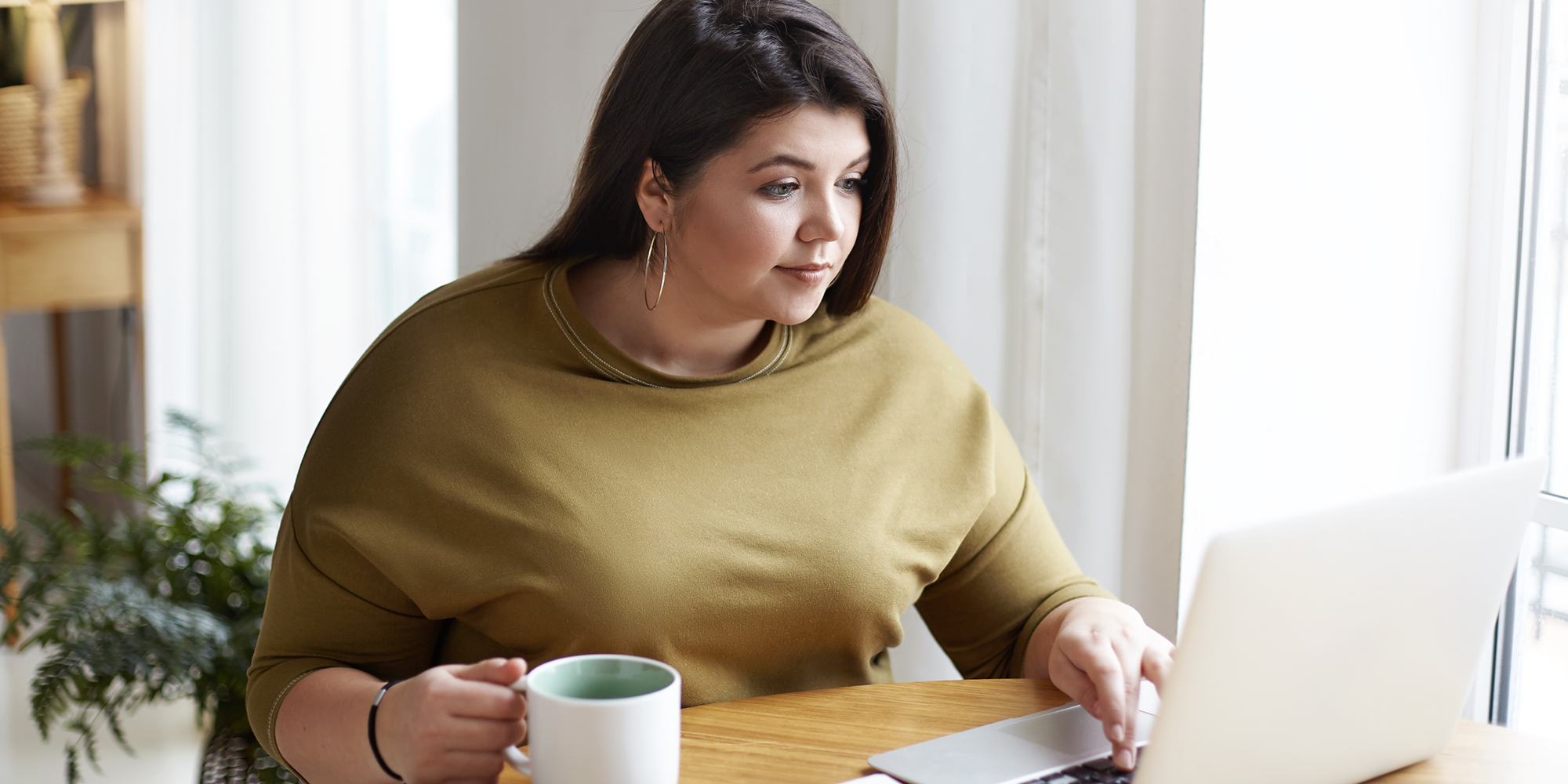 lady looking at her laptop drinking a cuppa