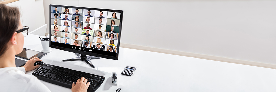 Lady looking at a screen full of faces on a video conference.