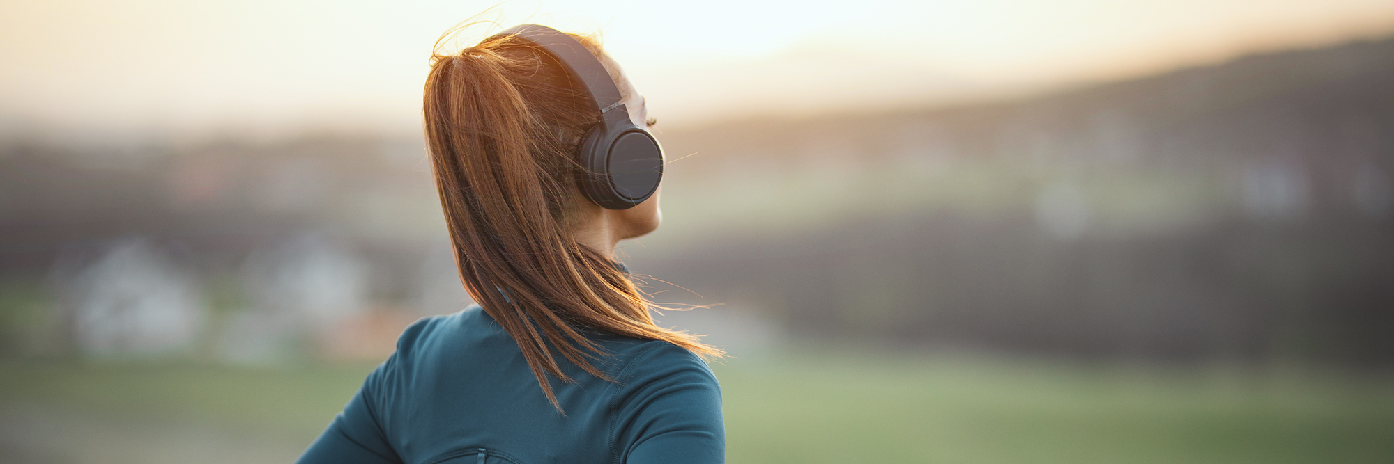 woman wearing headphones looking away from the camera into the field beyond with the sun setting | Digital Wings What is Digital Wellbeing