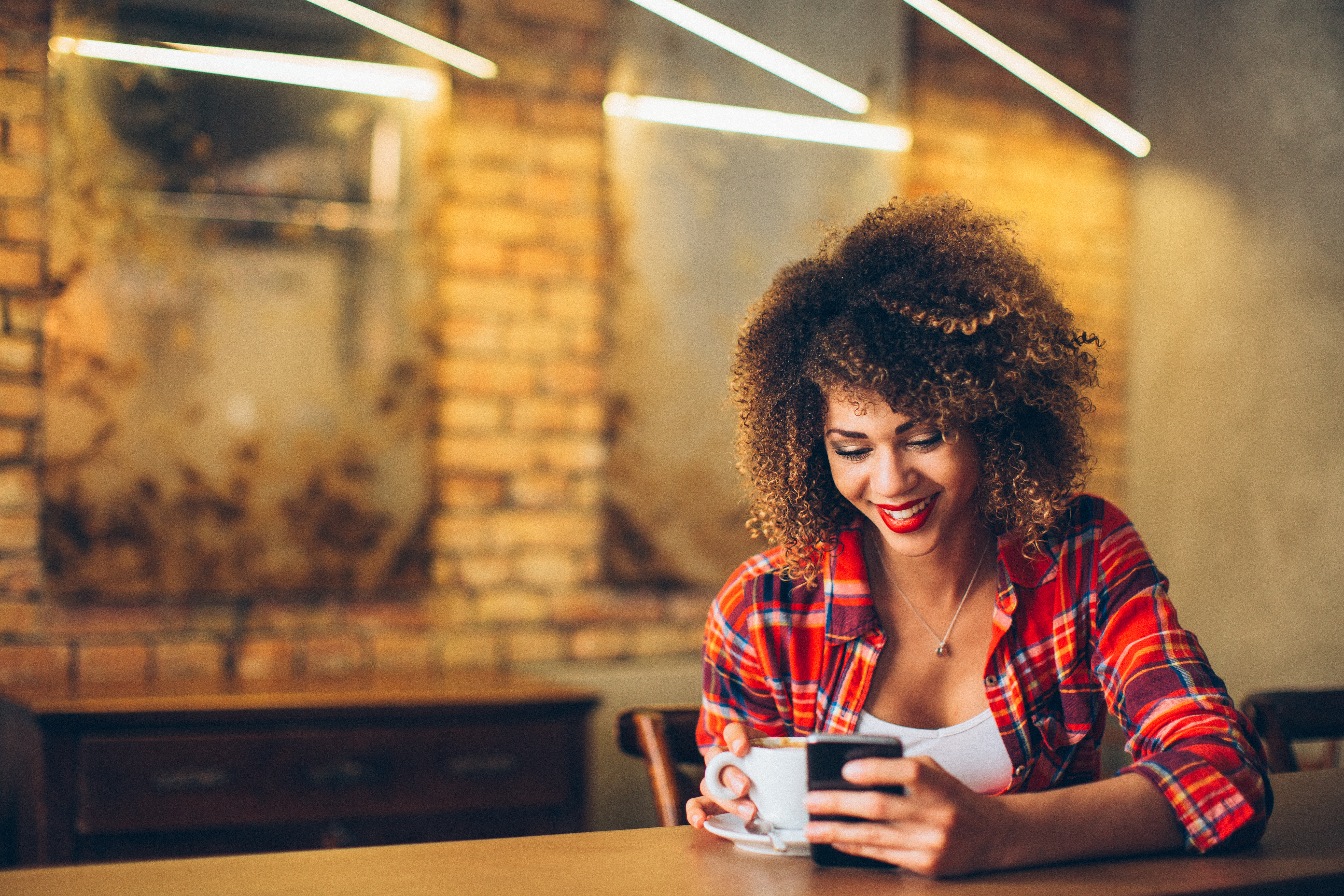 Young lady looking at her phone whilst holding a hot drink.