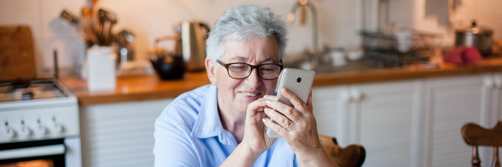 older lady sitting at her kitchen table smiling at her smartphone  | smartphone for a grandparent