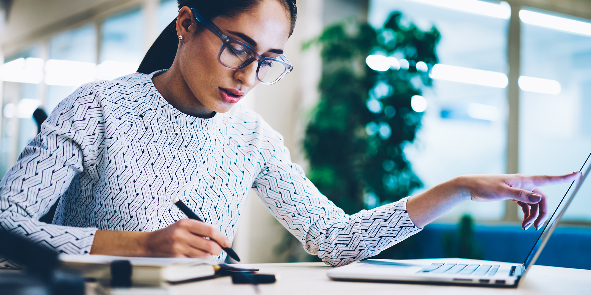 Woman pointing at her laptop whilst writing on a notepad | Digital Wings | Online money management