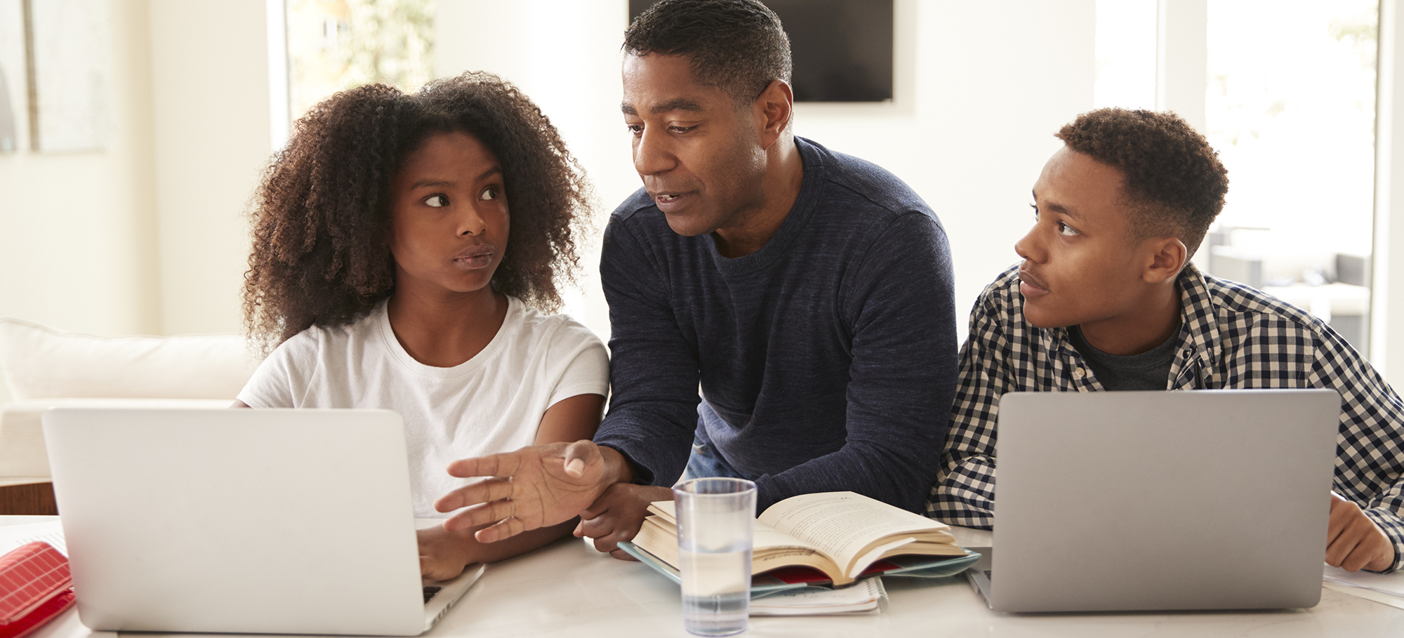 Man talking to his two children who are both using laptops.