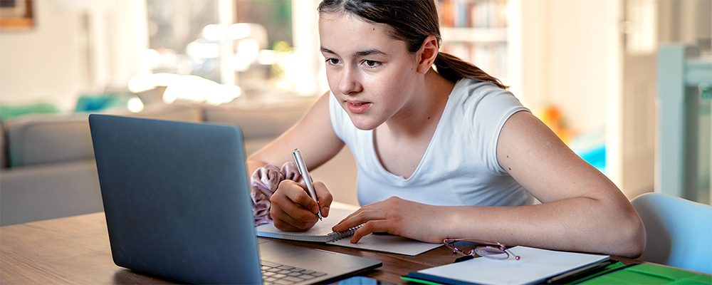 Child making notes while watching something on a laptop