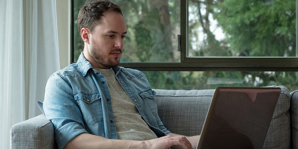 Man sitting on his sofa typing on his laptop