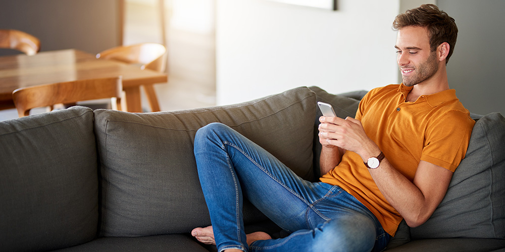 Man smiling while using his smartphone on the sofa