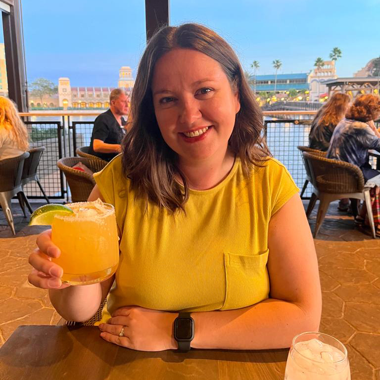 Rachael in a restaurant holding up her drink to the camera smiling