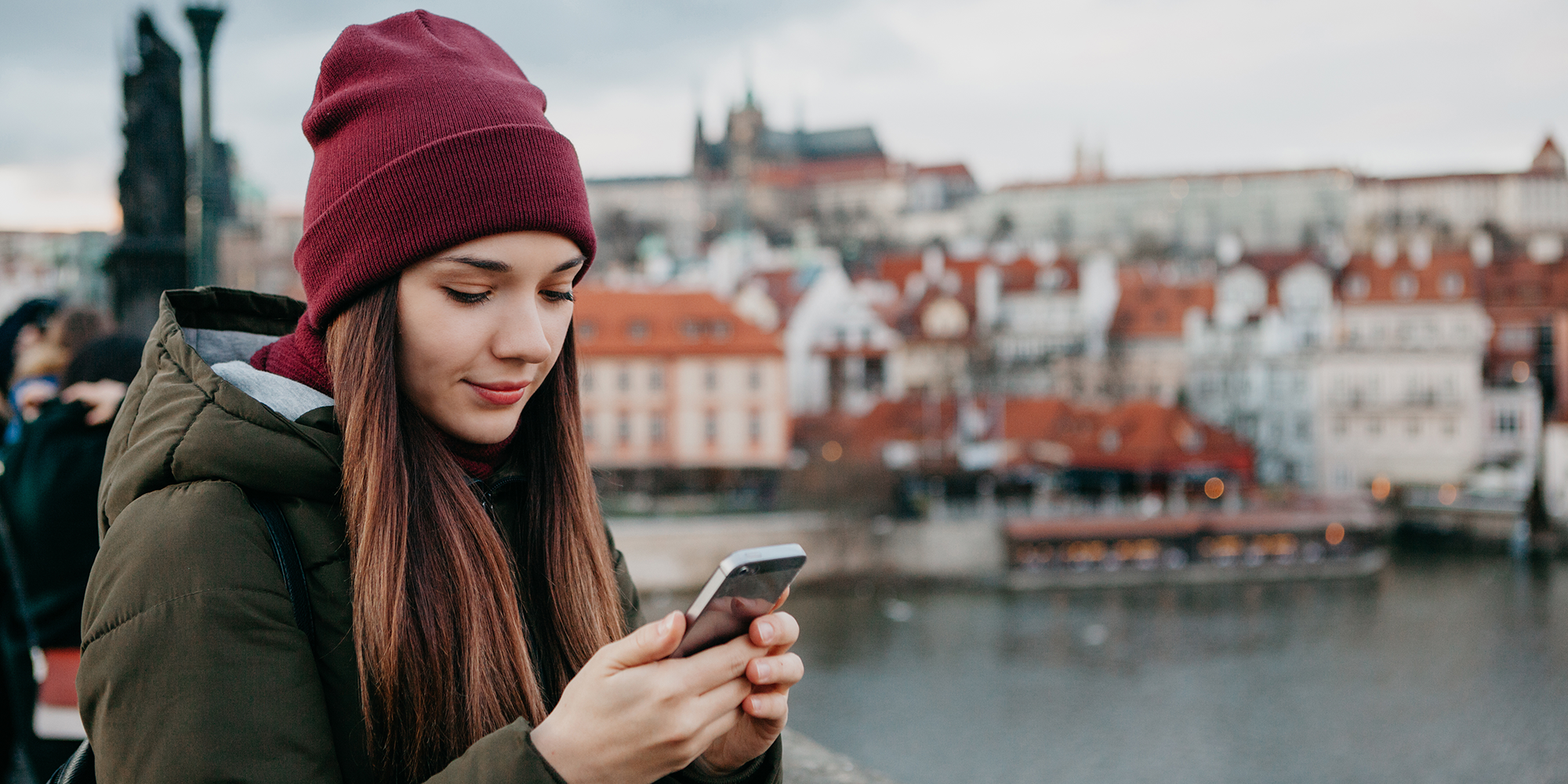 Girl using her smartphone standing next to a river in a city.