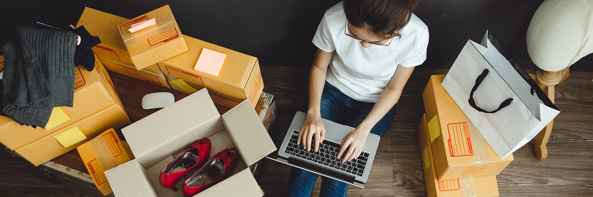 Woman sitting on the floor typing on a laptop surrounded by boxes | Digital Wings | Safe online shopping