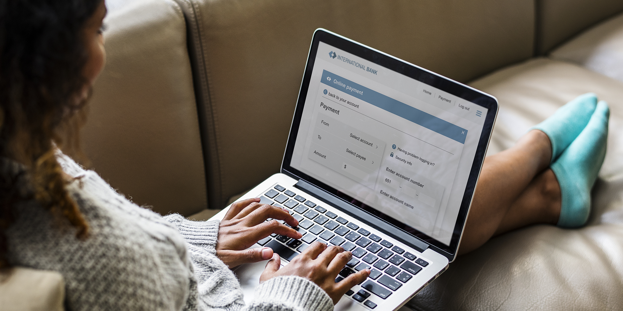 overhead image of a woman sitting on a sofa doing her online banking on a laptop | Digital Wings | Online money management