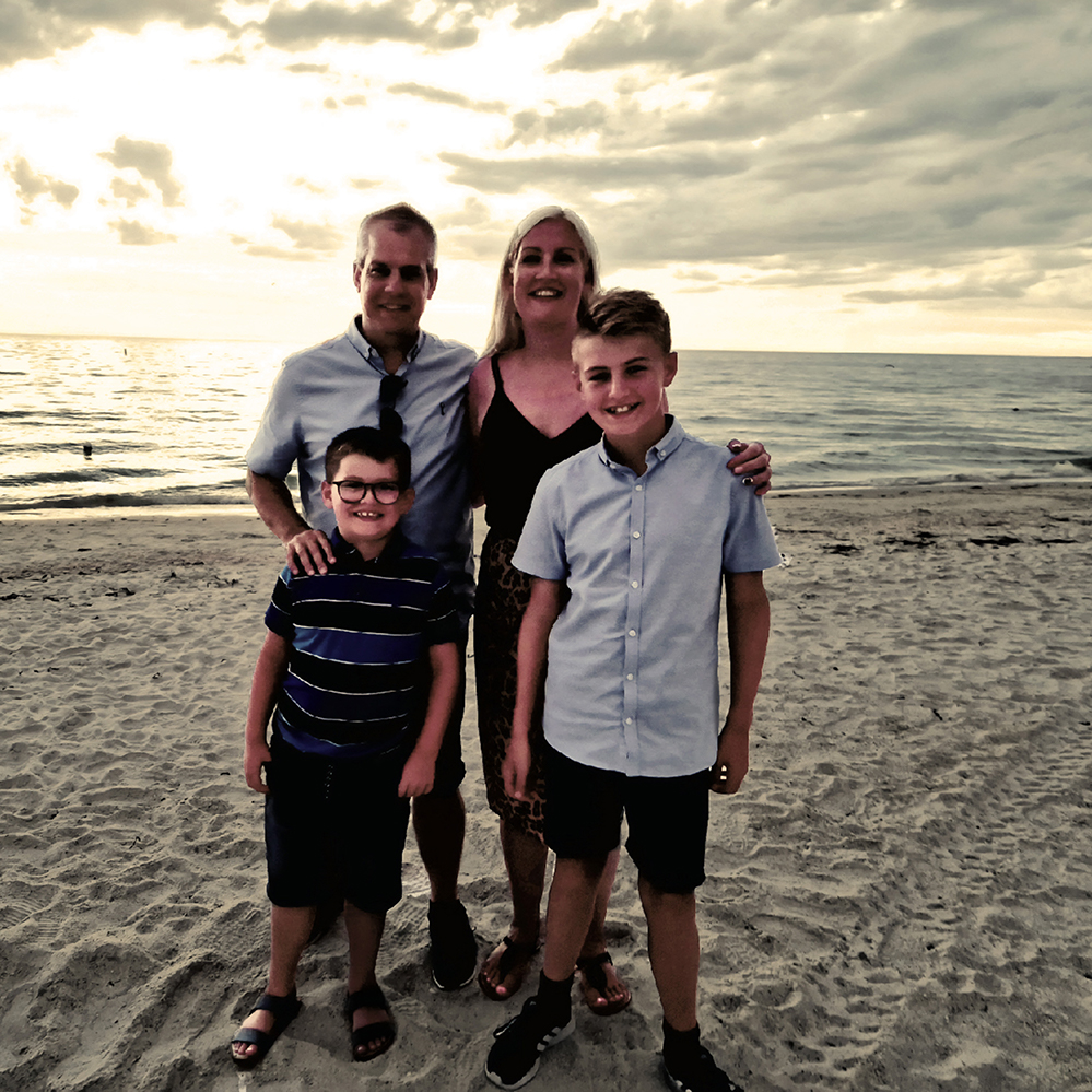 Matt with his wife and two sons standing on a beach at sunset