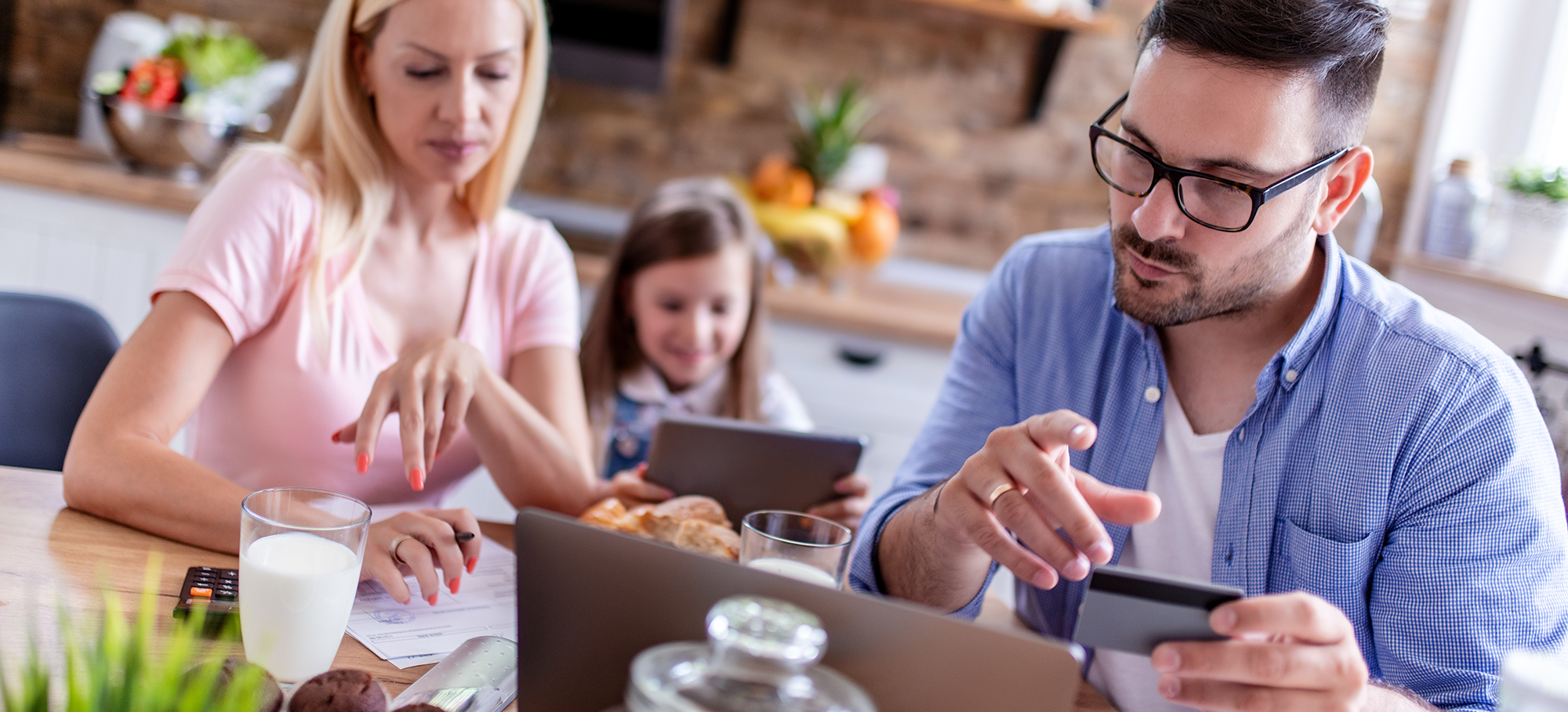 man, woman and child in a kitchen. the man is looking at his laptop holding a payment card | Digital Wings | Safe online shopping