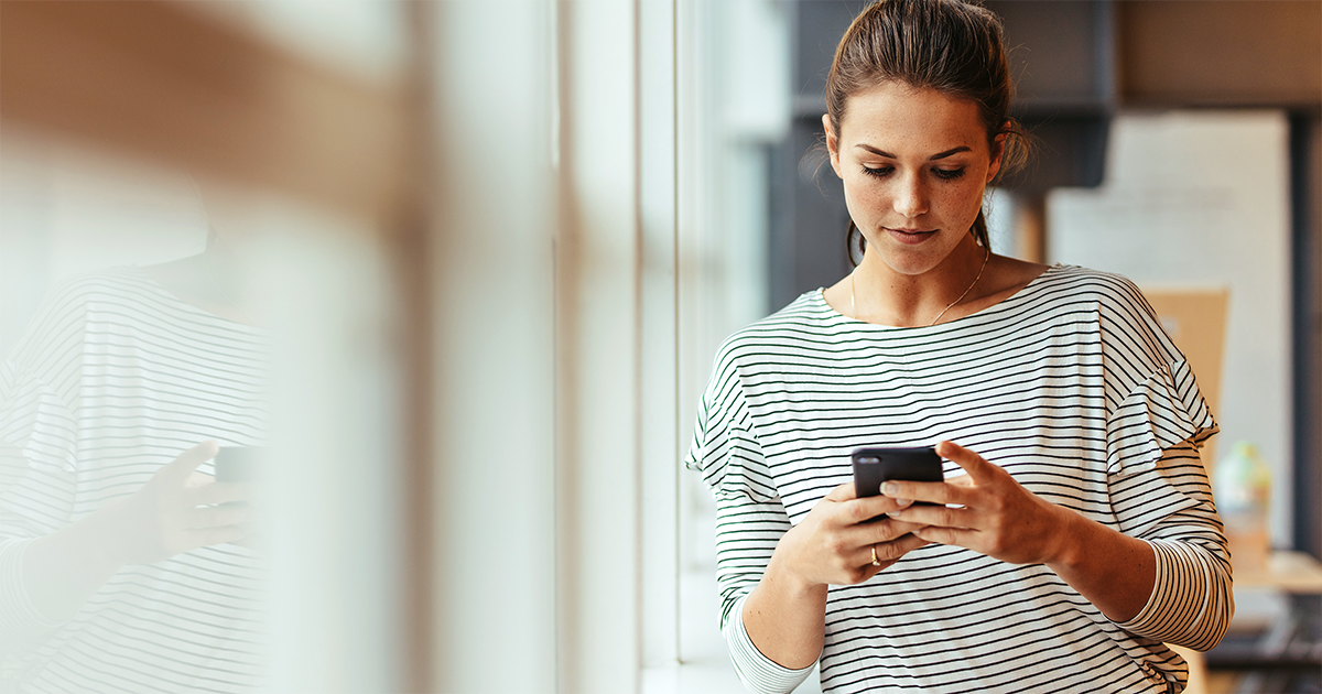 Lady looking at her phone, near a bright window.