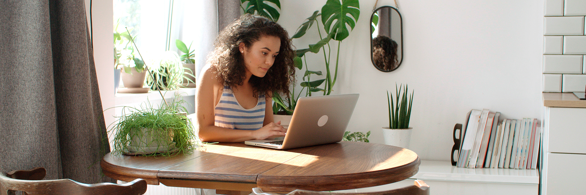 young woman in a room with lots of houseplants looking at her laptop  | Ultimate guide to Essential digital skills | Digital Wings blog
