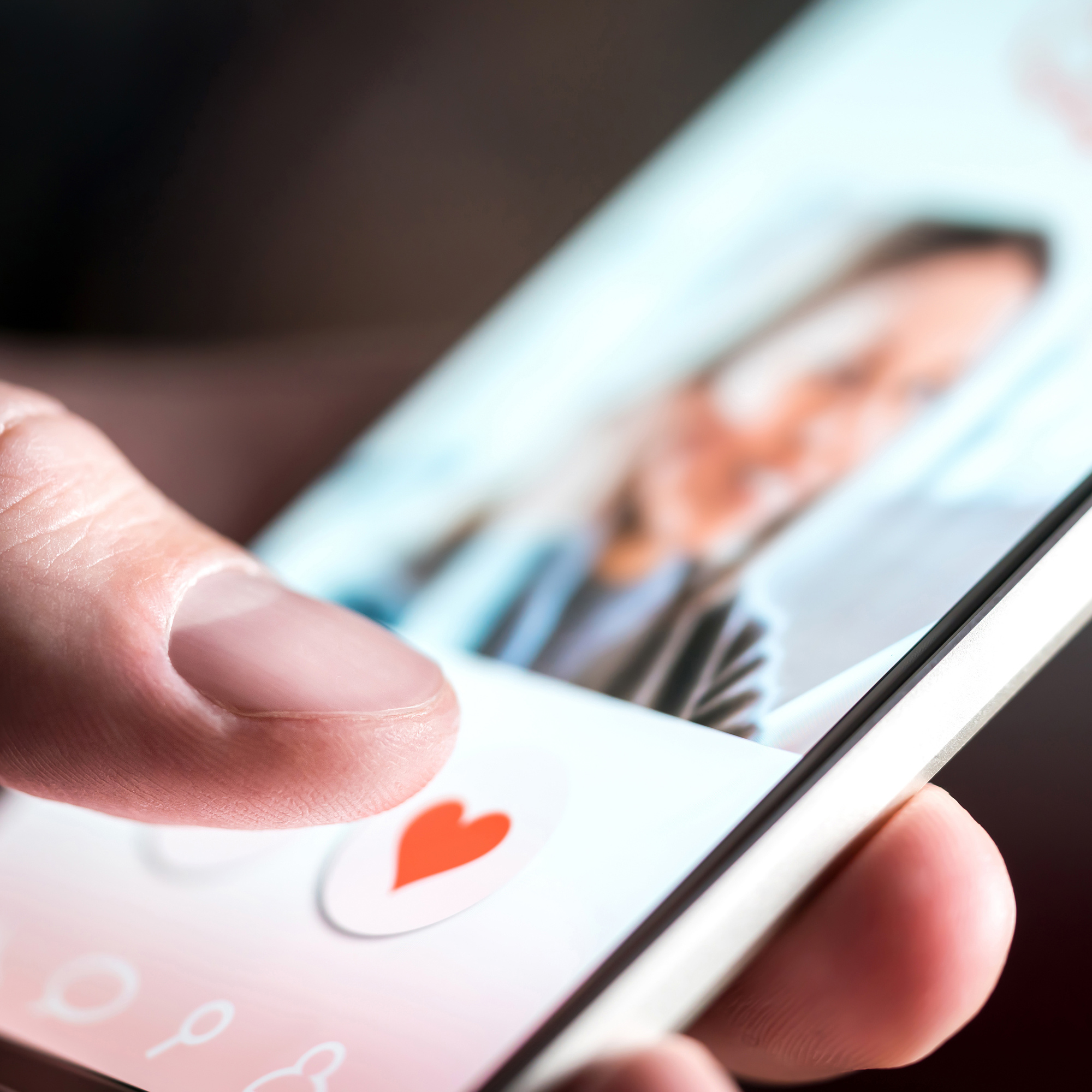 A close up image of someone's profile on a smartphone, the thumb of the person looking at the image has just tapped the red heart button on the screen as it's lit up.
