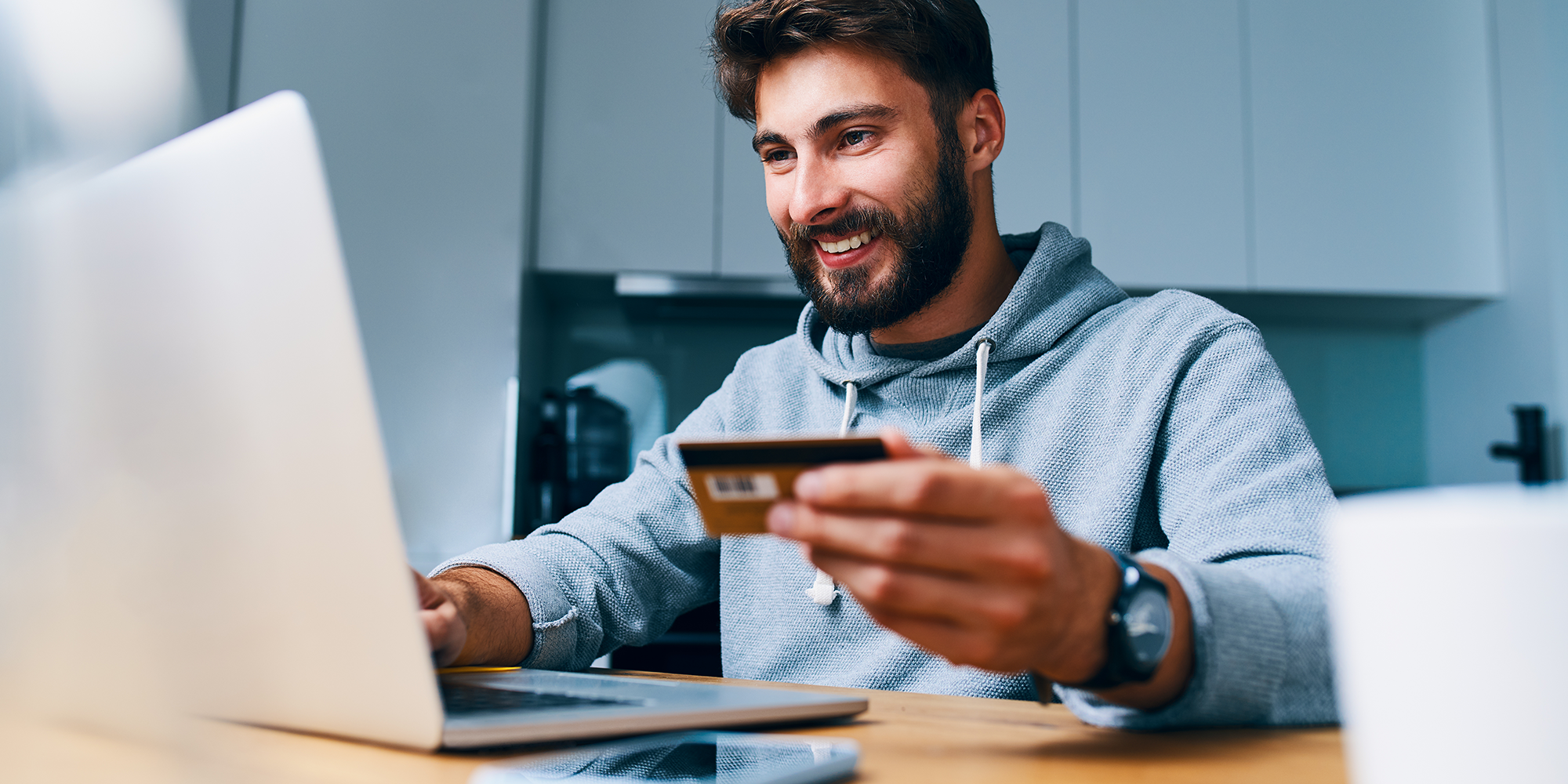 man holding a payment card smiling at his laptop | Digital Wings | Safe online shopping