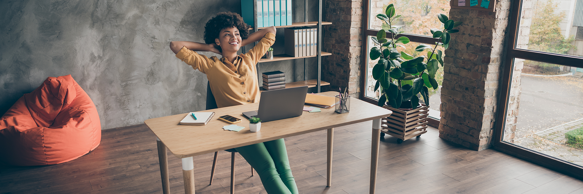 woman sitting at a desk with her hands behind her head and her legs stretched out.