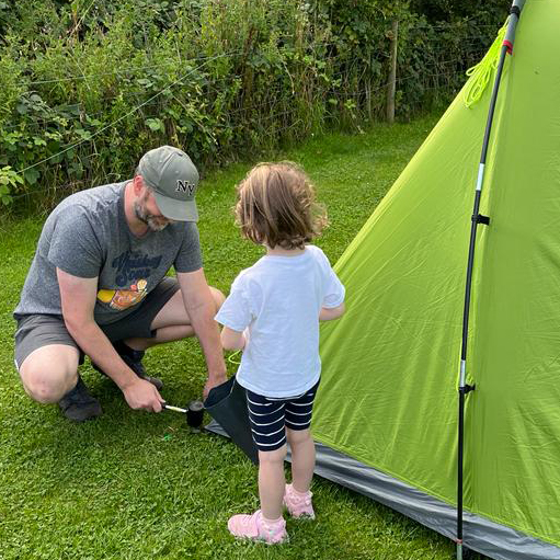 Andy tapping in tent pegs with his daughter helping him