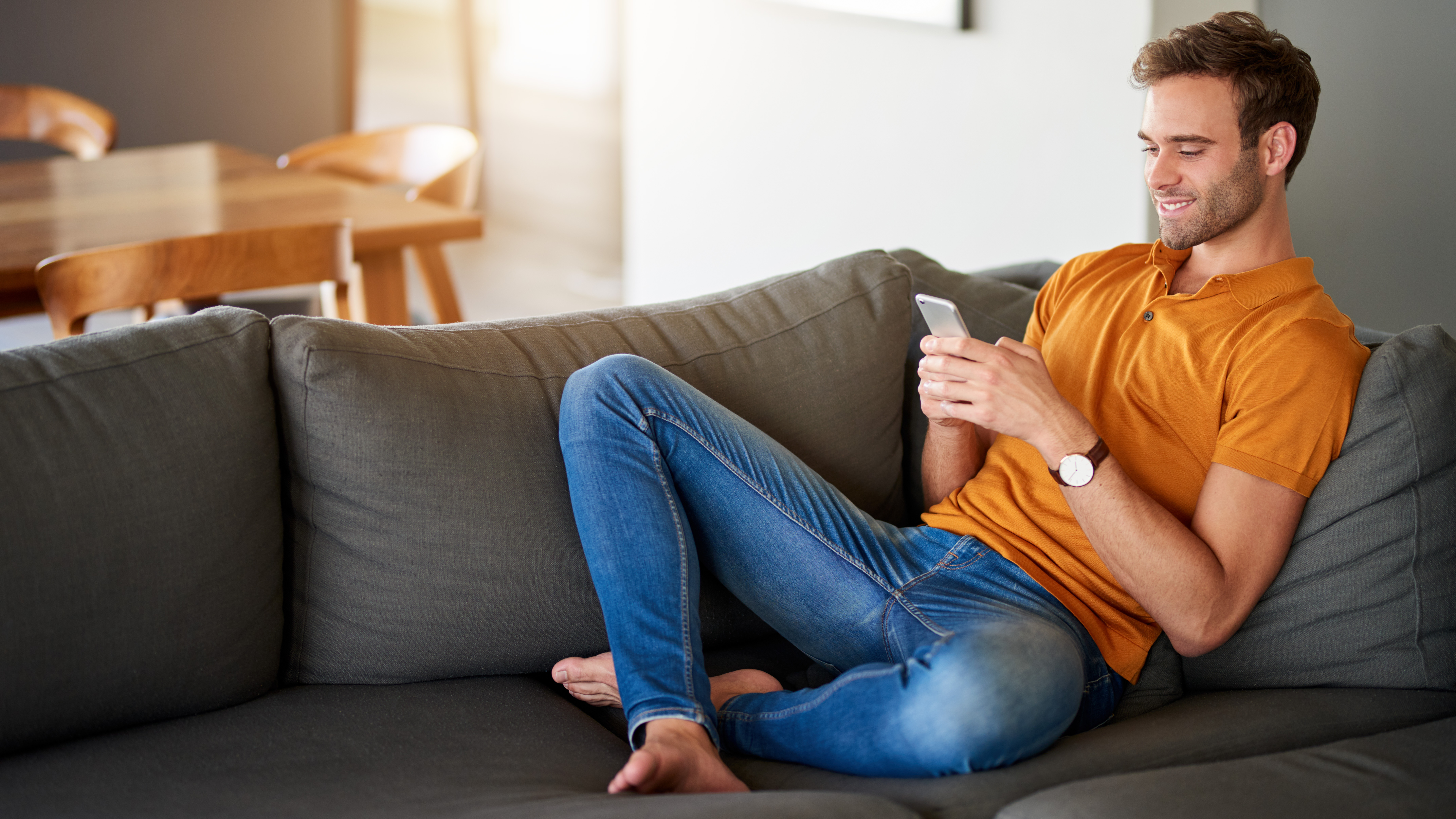 man sitting on his sofa smiling at his mobile phone | Keeping Safe Online - Ultimate Guide | Digital Wings