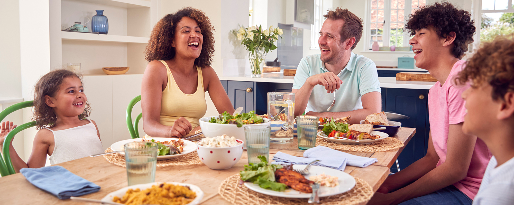 multi racial family sitting around a dinner table eating their dinner laughing and smiling together with no digital devices on the table | Digital Wings What is Digital Wellbeing