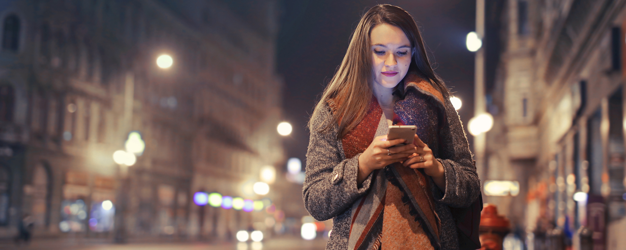 Person using mobile phone in a dimly lit city street.